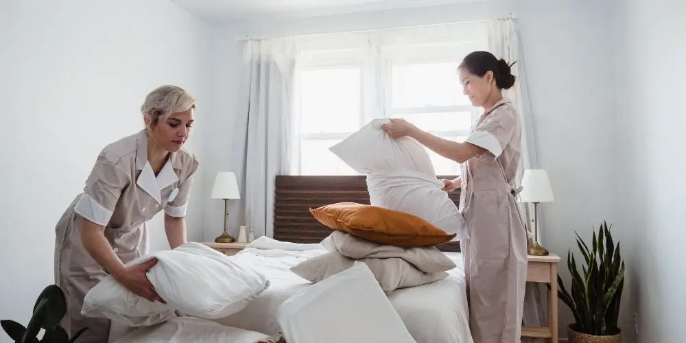 Duas camareiras arrumando travesseiros de uma cama de hotel