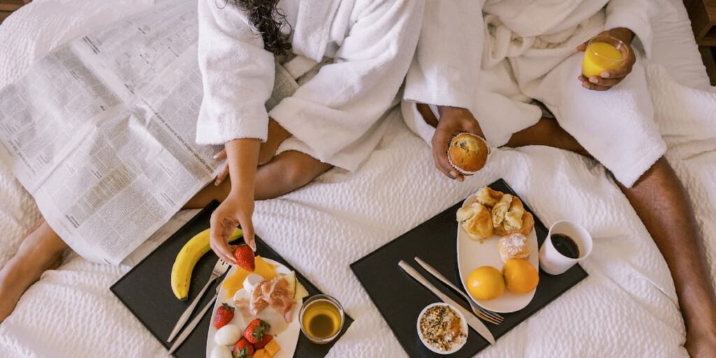 Imagem de um casal na cama com bandejas de café da manhã