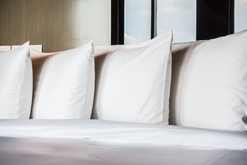 Cama de hotel com quatro travesseiros brancos alinhados e enxoval branco.