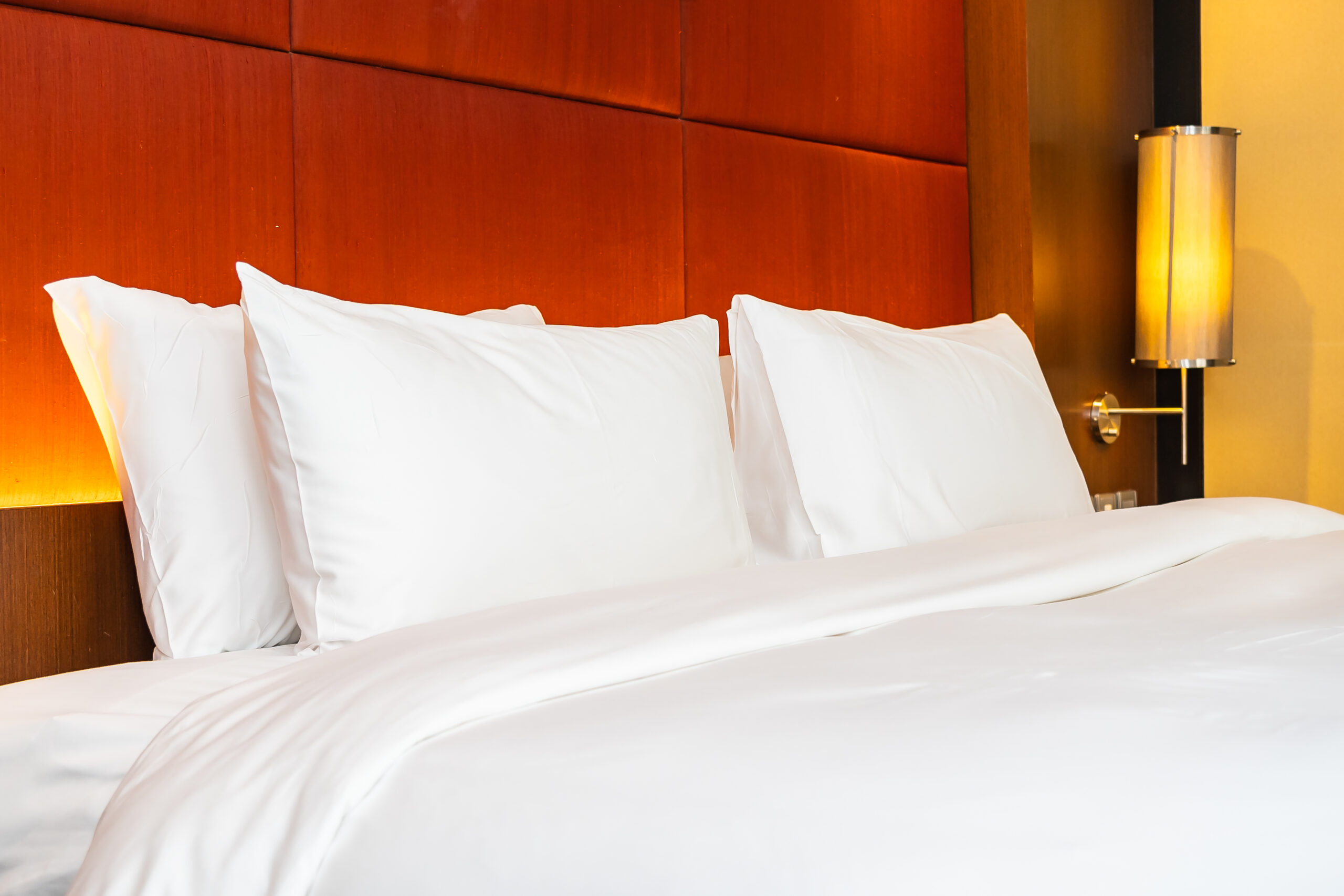 Detalhe de cama arrumada com enxoval branco e iluminação aconchegante ao lado da cabeceira.