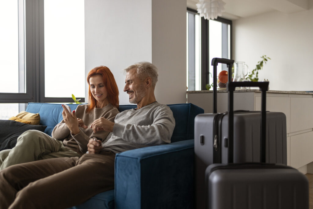 Casal sentado em sofá moderno com malas ao lado, relaxando após o check-in em hospedagem. A atmosfera acolhedora e bem iluminada sugere conforto e satisfação durante a estadia.